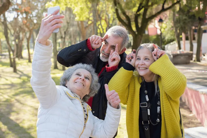 Drei ältere Freunde machen im Park ein Selfie und schneiden Grimassen