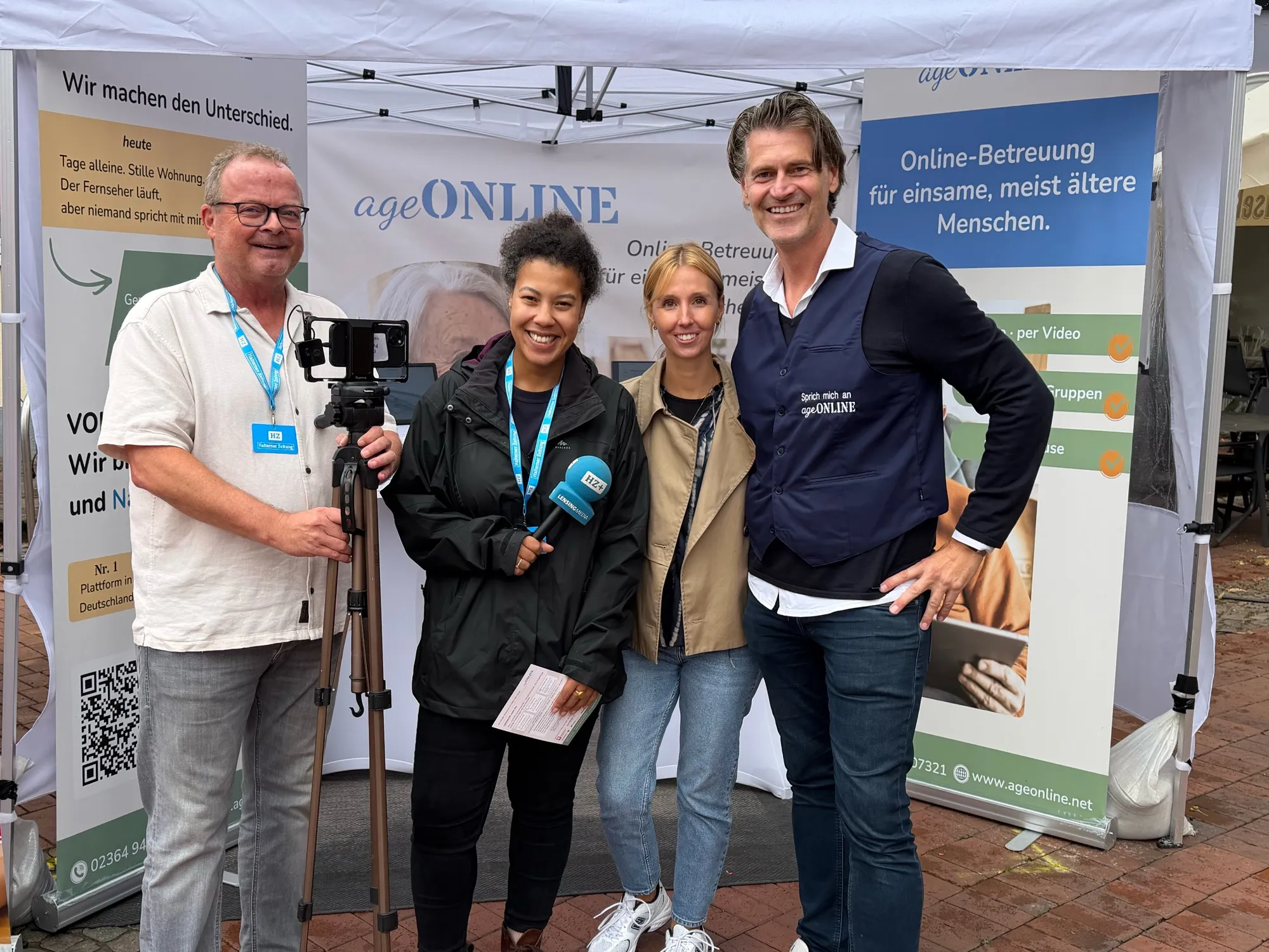Vier Personen stehen lachend vor dem ageONLINE-Stand, vorn eine Kamera auf einem Stativ und ein Mikrofon der Halterner Zeitung
