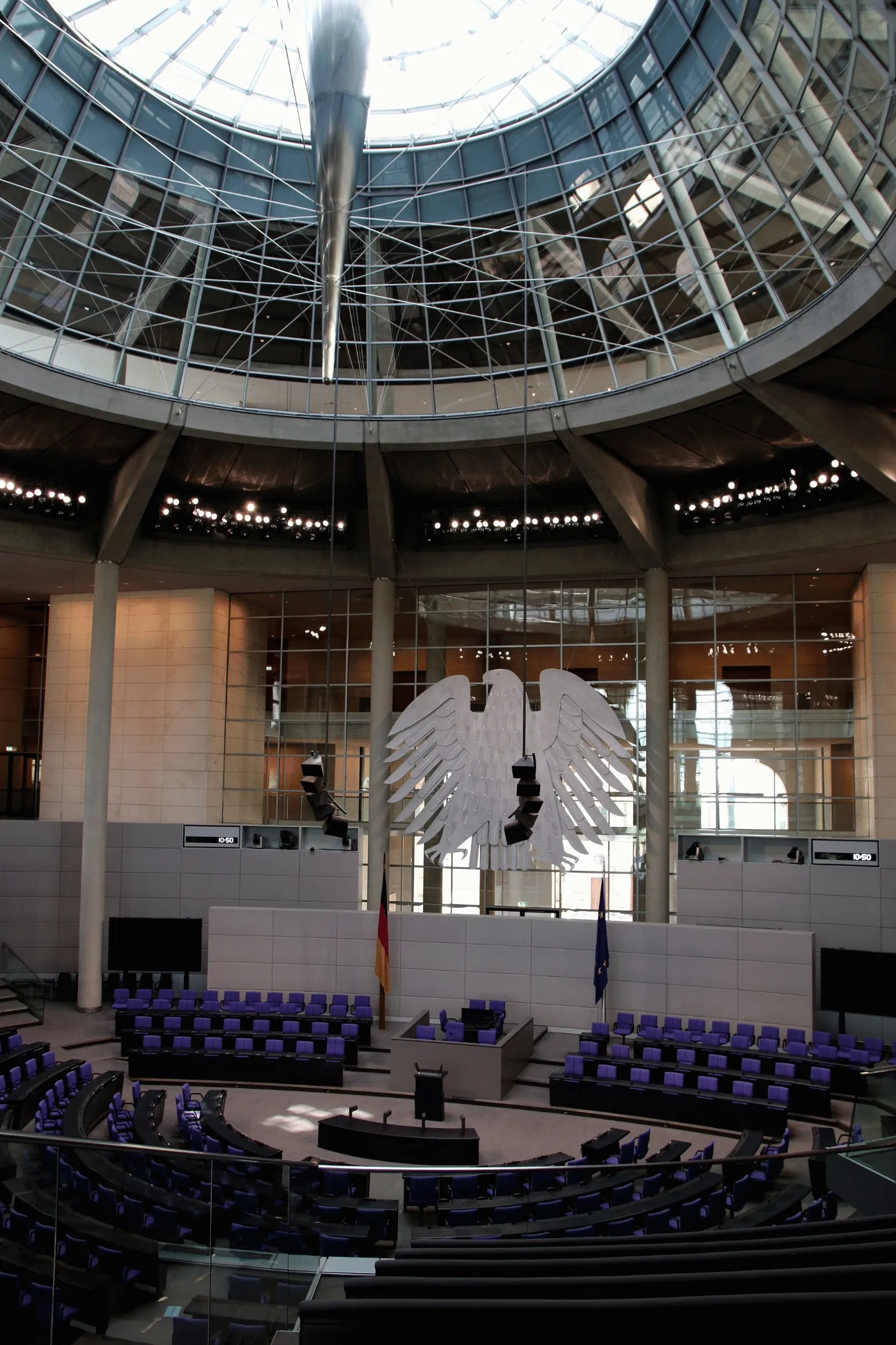 Der Plenarsaal des Deutschen Bundestages mit blauen Sitzreihen, Bundesadler und Glaskuppel.