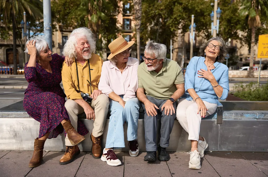 Fünf ältere Menschen sitzen nebeneinander auf einer Mauer und lachen