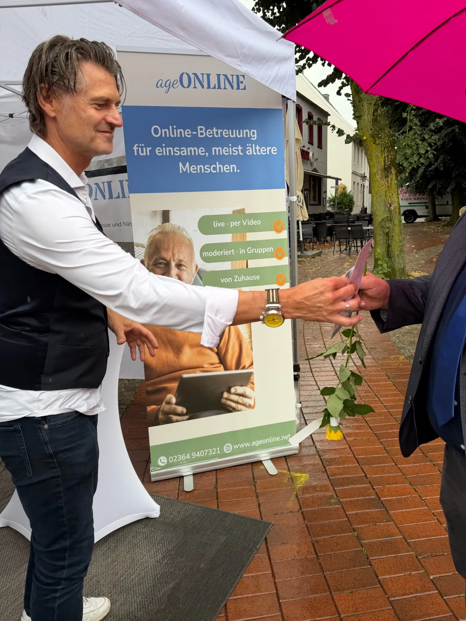 Am ageONLINE-Stand bekommt Bürgermeister Andreas Stegemann unter einem pinken Regenschirm einen Flyer gereicht