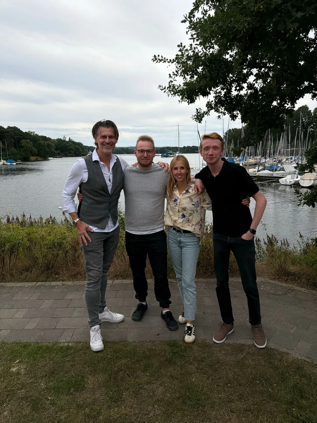 Vier Mitglieder des ageONLINE-Teams stehen Arm in Arm vor einem Segelhafen am See